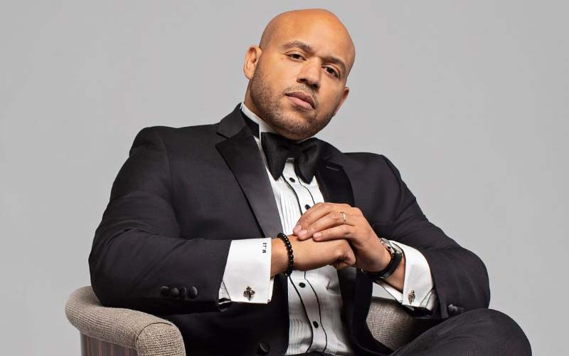 A bald man in a suit and tie sitting on a chair.